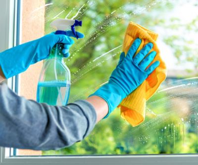 Tiefenreinigung für dein Zuhause, Hand mit Putzhandschuhen und Glasreiniger putzt Fenster