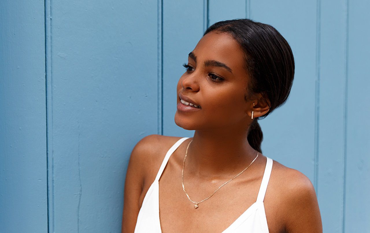 Femme aux cheveux bruns et lissés posant devant un mur bleu