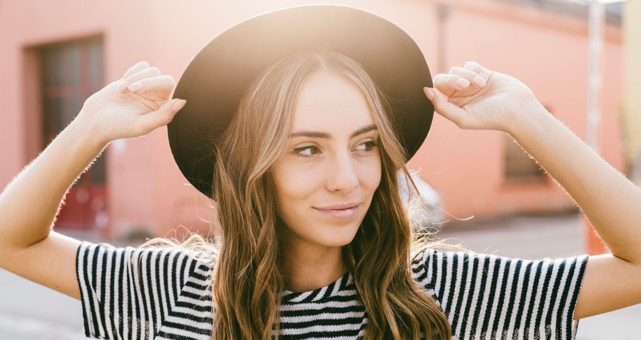 Femme aux longs cheveux châtains avec un chapeau noir et un pull rayé 