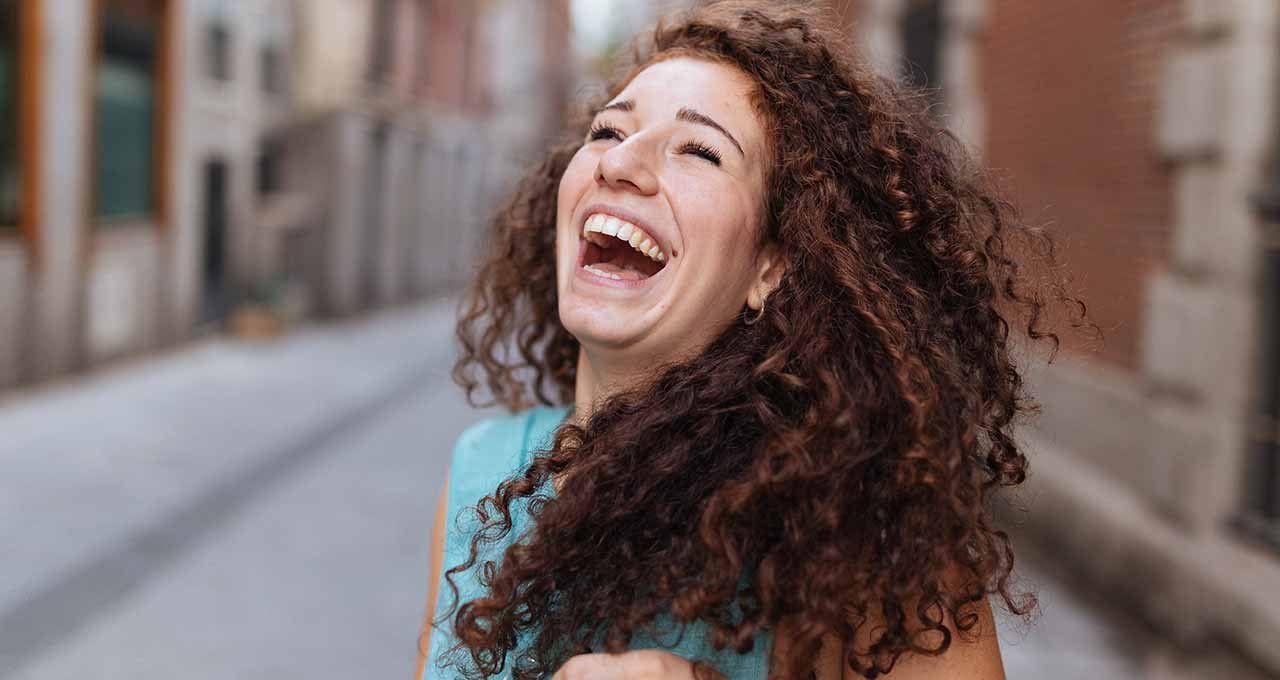 Femme rousse aux cheveux naturellement bouclés en train de rire aux éclats