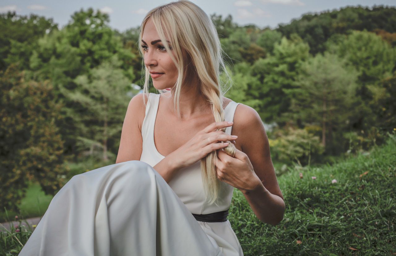 Femme blond portant une robe blanche en train de se tresser les cheveux