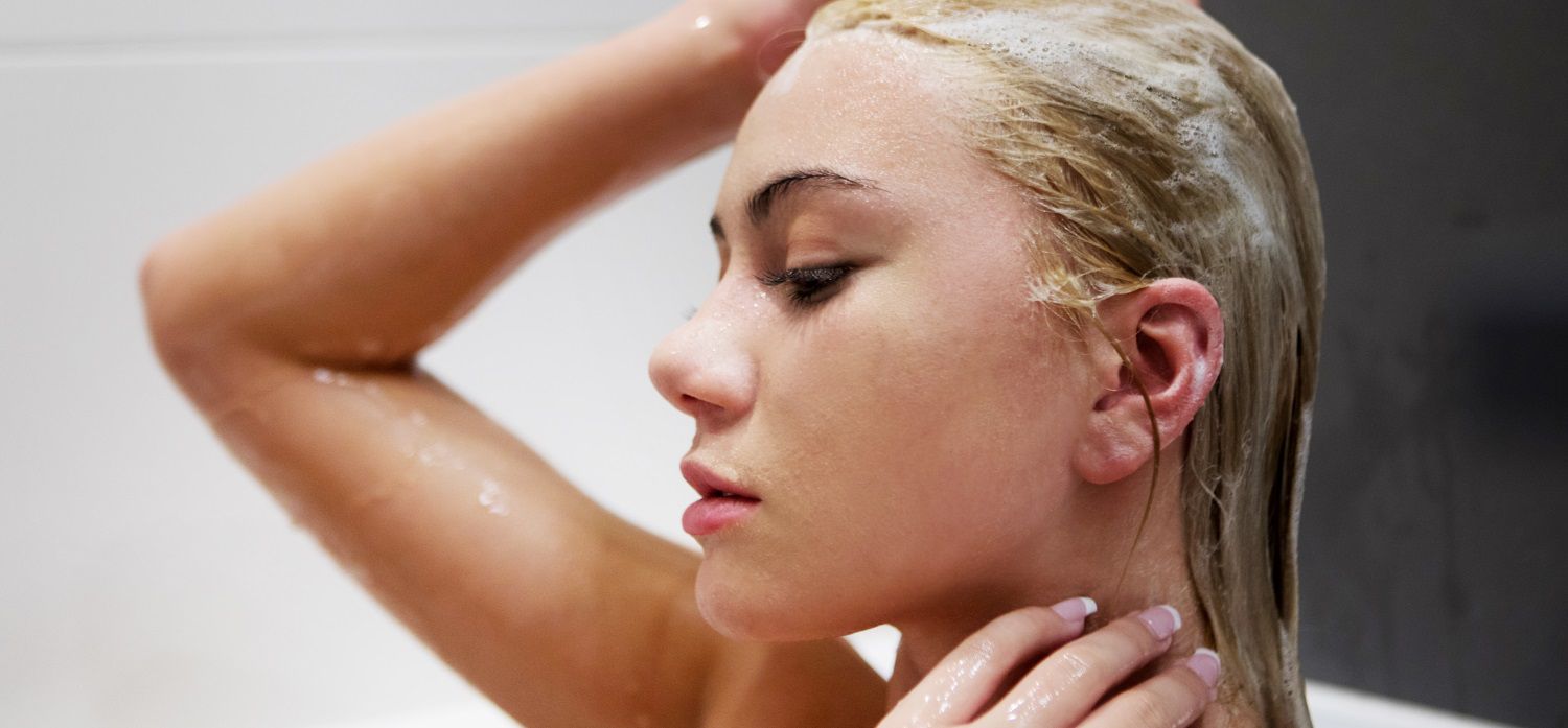 Femme blonde en train de se laver les cheveux avec du shampooing 
