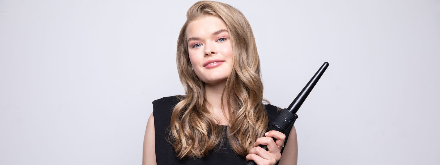 Blonde woman with wavy hair, holding a curling wand.