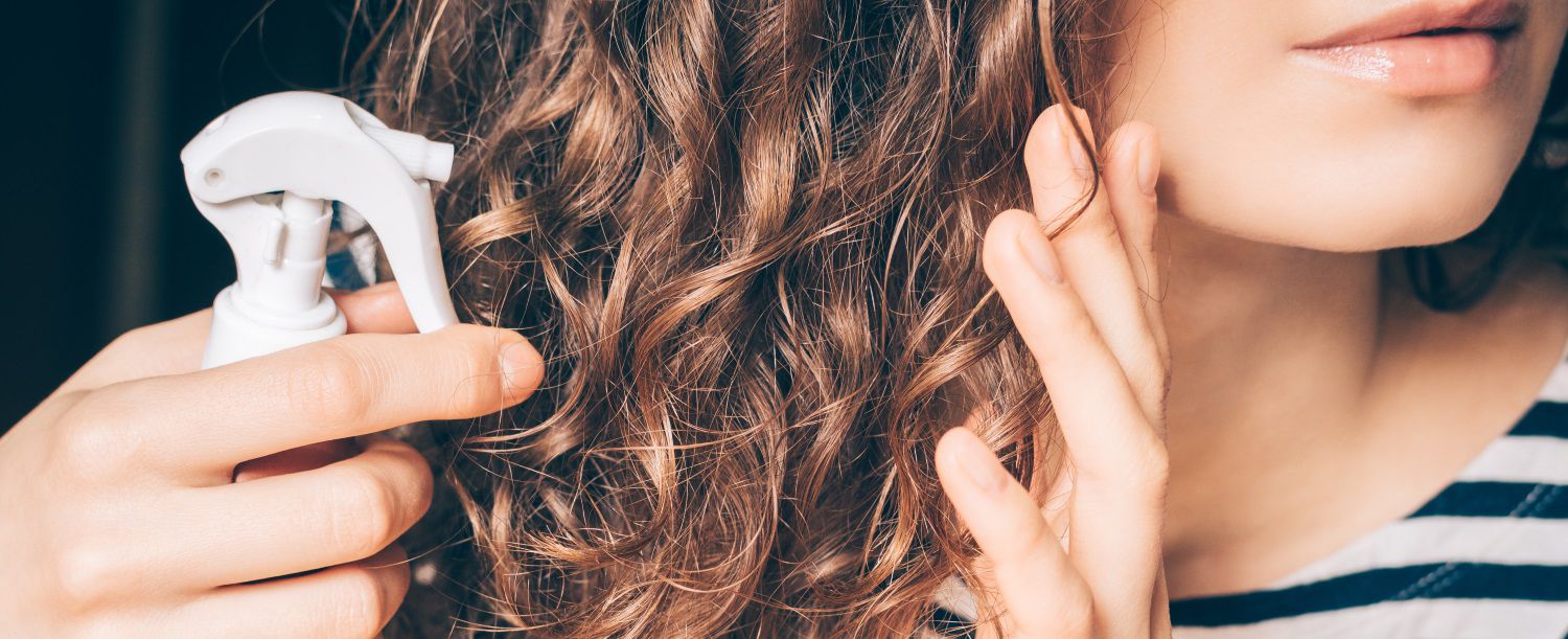 Close-up sulla capigliatura riccia di una donna che si appresta a spruzzare un prodotto per capelli