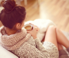 Brunette woman with messy bun curled up on the sofa holding a hot drink