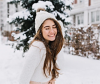 Brunette woman wearing white plays in the snow as snowflakes fall