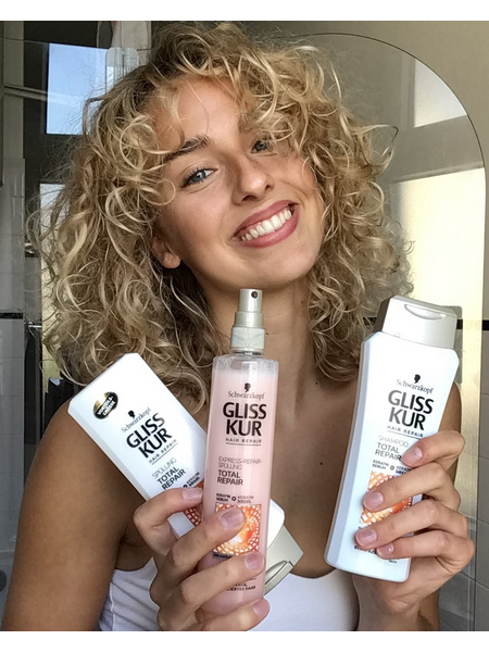 Woman with gorgeous curly hair, holding Gliss Total Repair products