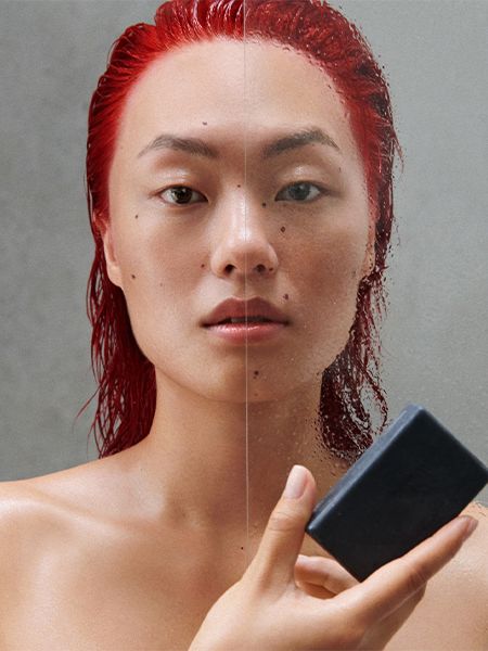 Woman with wet red hair stands in shower and holds a Shampoon Bar