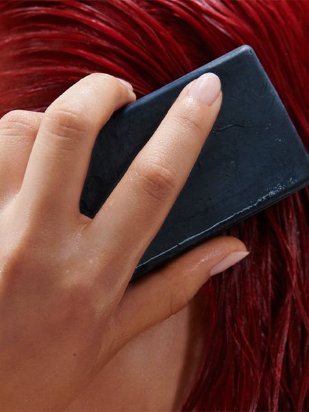 Close up of a hand rubbing the Shampoon Bar through wet red hair