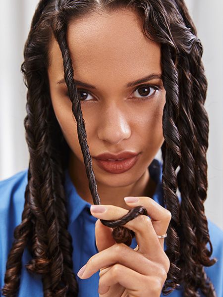 Woman looks into the camera while twisting a strand of her hair to form curls