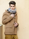 Man with slicked back dark brown hair wears light brown toggle jacket and oversized scarf in front of beige background