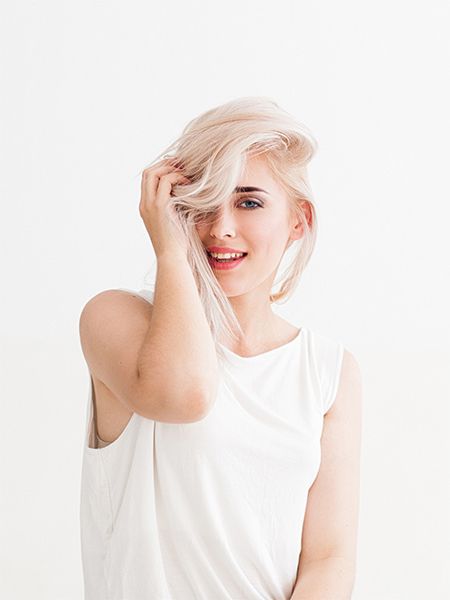 Žena s platinovými blond vlasmi v bielom top sa dotýka jej vlasov.
