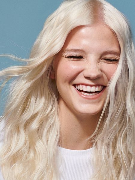 Young woman with long, blonde hair, and white top, laughing. 