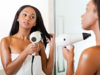 Black-haired woman blow-drying her hair in front of a mirror