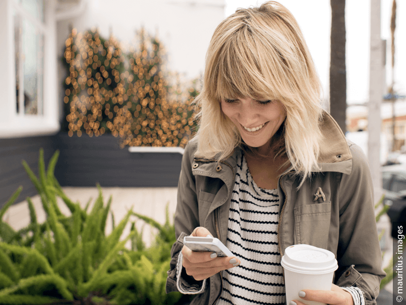 Blond woman with modern zigzag part holding a coffee cup and a smartphone