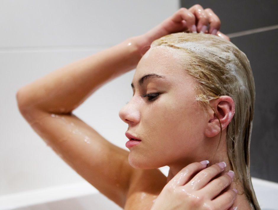 Femme blonde en train de se laver les cheveux avec du shampooing 