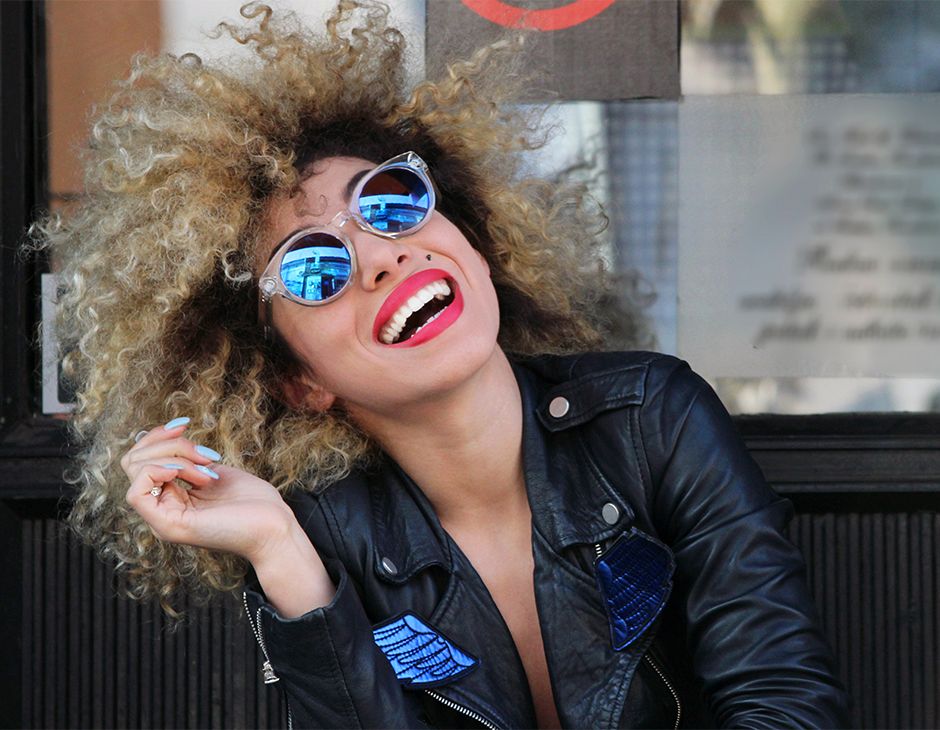 Femme souriante avec des lunettes de soleil et des cheveux bouclés.