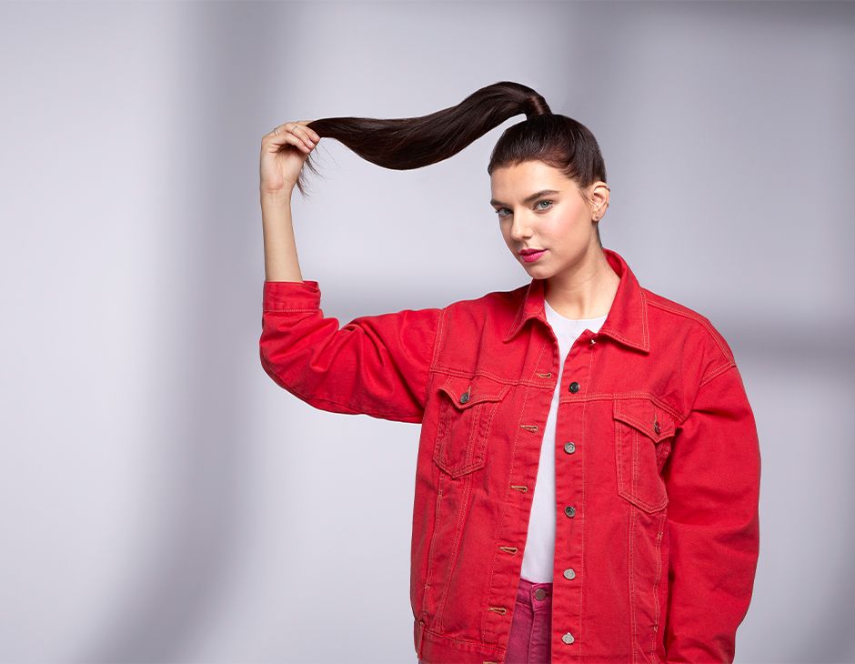 Темноволосая девушка держит в руке длинный конский хвост