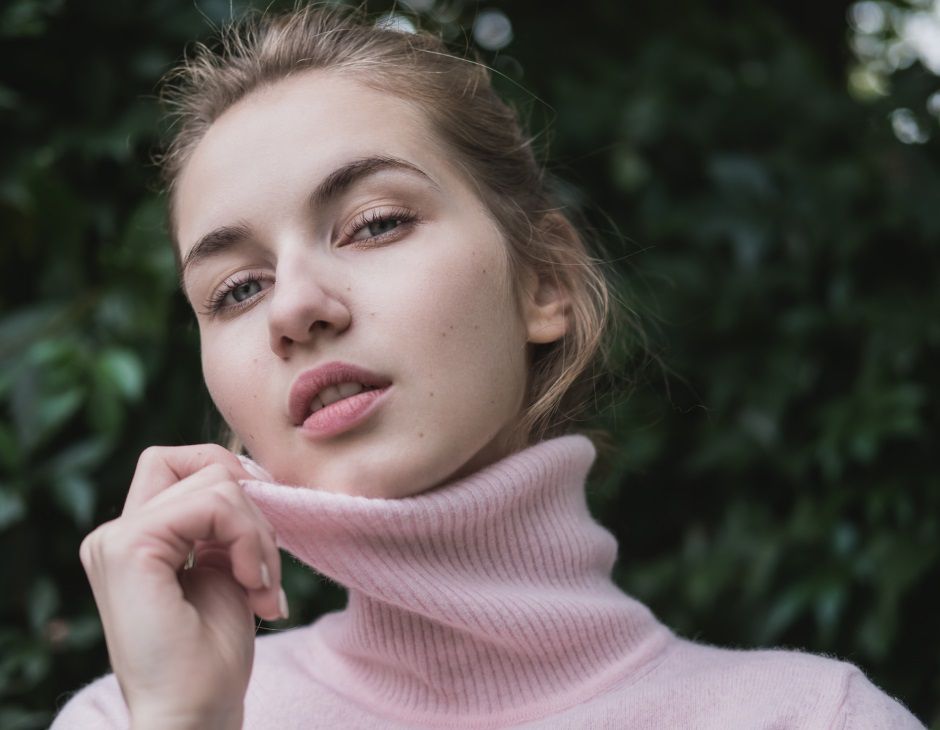 Femme blonde avec un chignon banane et un pull à col roulé rose 