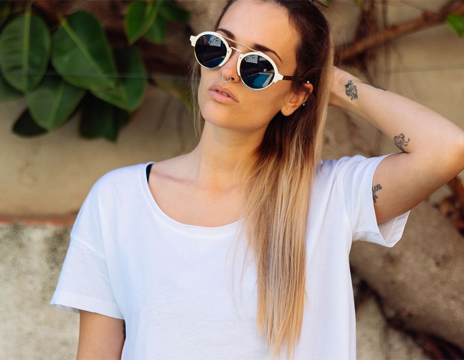 Женщина в белой футболке и солнцезащитных очках с окрашиванием балаяж на длинных волосах.