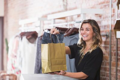 smiling woman working in a clothing store holding a paper bag in her hands