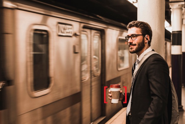 地铁旁站着一位手拿咖啡杯的男士