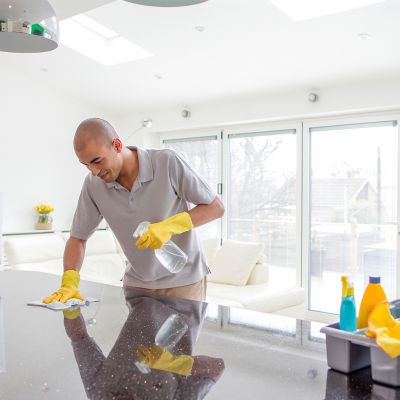 man cleaning a shiny kitchen with several cleaning products