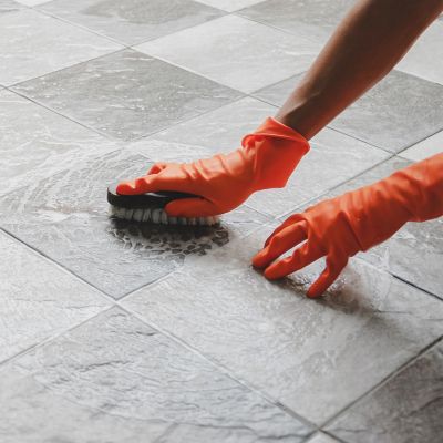 Osoba nosząca czerwone rękawiczki czyszcząca podłogę w łazience