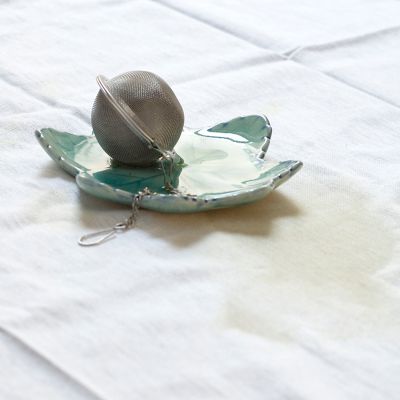Zaparzaczka do herbaty leżąca na zielonej podstawce na białej tkaninie