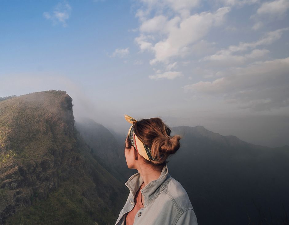 Femme brune vue de dos avec un bandeau et un chignon dans les cheveux en face d’une montagne