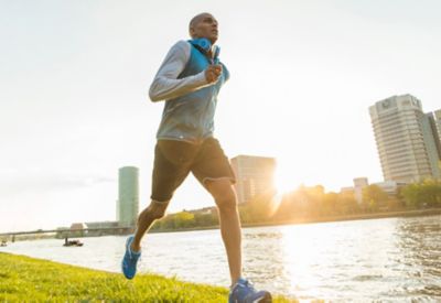 Un joggeur court au bord d'une rivière au coucher du soleil