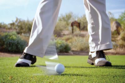 pés de uma pessoa em um campo de golfe, balançando um taco