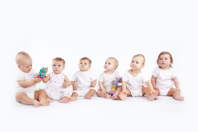 seis crianças pequenas usando roupas brancas sentadas em fila olhando para algo ao lado da câmera