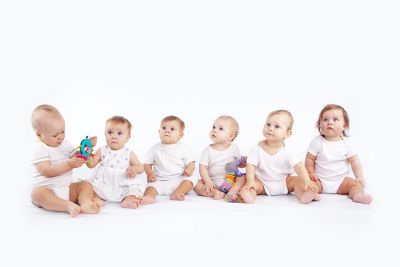 six little children wearing white clothes sitting in a row looking to something next to the camera