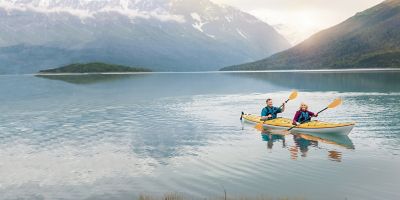 elderly couple sitting in a canoe on a lake with mountains in the background