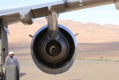 Mechanic standing behind wheel near engine and beneath wing of a parked airplane with desert background