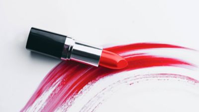 Roter Lippenstift ohne Kappe liegt auf einem dicken, zum Halbkreis gebogenem, roten Streifen, der mit einem Lippenstift gemalt wurde. 