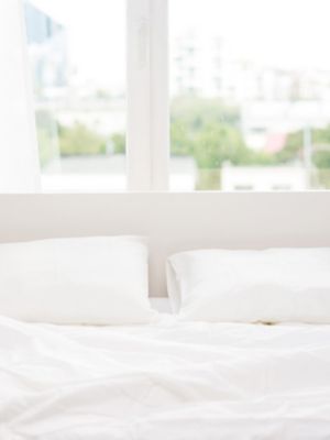 Un pat cu cearceafuri albe de in, poziționat în fața unui geam.