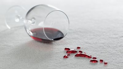 Un pahar de vin roșu răsturnat, pe covorul roșu câteva pete de vin. 