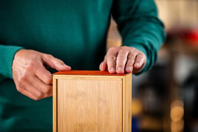 Uma caixa de madeira com couro em uma das laterais. Duas mãos aparecem pressionando o couro colado.
