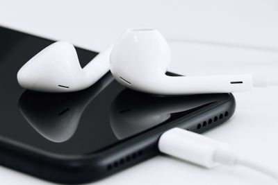 Closeup photo of white earphones plugged into a black cell phone on a white surface shutterstock ID 506932279