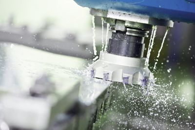 Primo piano di un centro di lavoro CNC che versa fluidi di lavorazione su un pezzo in metallo.