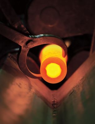 Piece of hot metal in the shape of a cylinder that is being held by pliers during the forging process