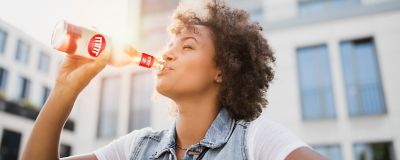 woman drinking from a labeled glass bottle with sun light in the background