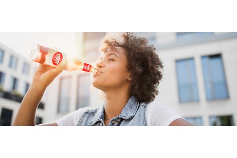 女子使用一个带标签的玻璃瓶饮用饮品，背景带有阳光。