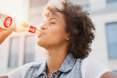 女子使用一个带标签的玻璃瓶饮用饮品，背景带有阳光。