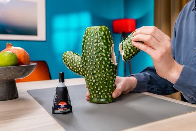 A hand applies Loctite Super Glue Gel from a tube to a broken ceramic cactus.
