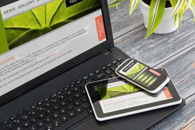 Photo of laptop, tablet and mobile phone with illustration of same web design on screen of all three devices