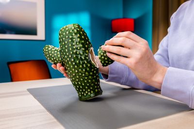 A woman holding the two parts of a broken ceramic cactus, positioning the broken piece in place.