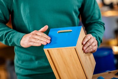 Two hands holding a wooden drawer with blue leather front.
